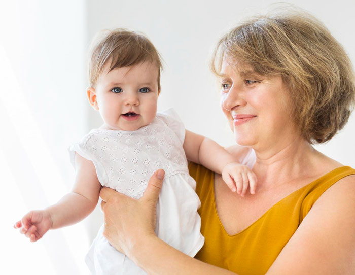 Woman in a mustard top holding a baby girl in white dress smiling, representing mil calls herself mommy theme Woman in a mustard top holding a baby girl in white dress smiling, representing mil calls herself mommy theme