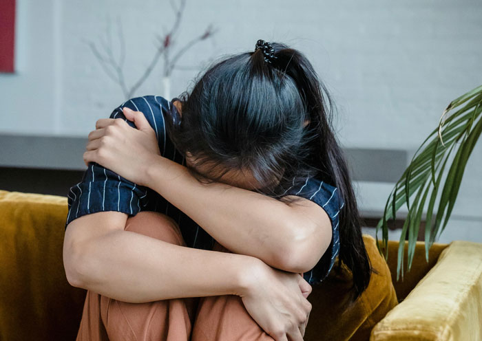 Young woman hugging knees while sitting on couch, feeling overwhelmed as mil calls herself mommy in tense moment Young woman hugging knees while sitting on couch, feeling overwhelmed as mil calls herself mommy in tense moment