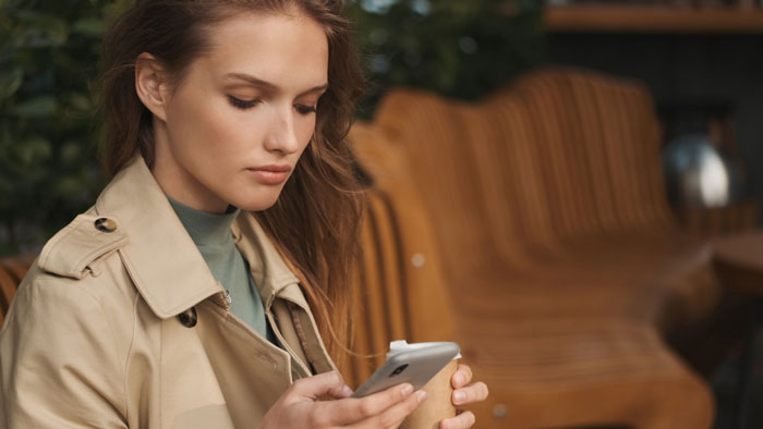 Young woman in a trench coat looking at her phone, concerned about MIL expecting DIL to pay for birthday dinner at fancy restaurant. Young woman in a trench coat looking at her phone, concerned about MIL expecting DIL to pay for birthday dinner at fancy restaurant.