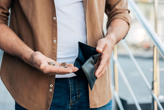 Man holding empty wallet and few coins, symbolizing financial stress related to paying for fancy restaurant dinner. Man holding empty wallet and few coins, symbolizing financial stress related to paying for fancy restaurant dinner.