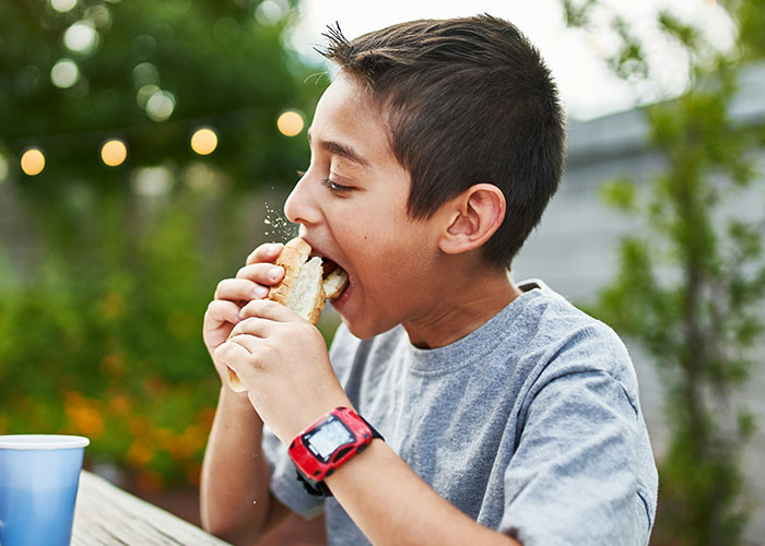 Boy wearing a red watch eating fast food outdoors, highlighting concerns about kids being fed unhealthy meals by MIL. Boy wearing a red watch eating fast food outdoors, highlighting concerns about kids being fed unhealthy meals by MIL.