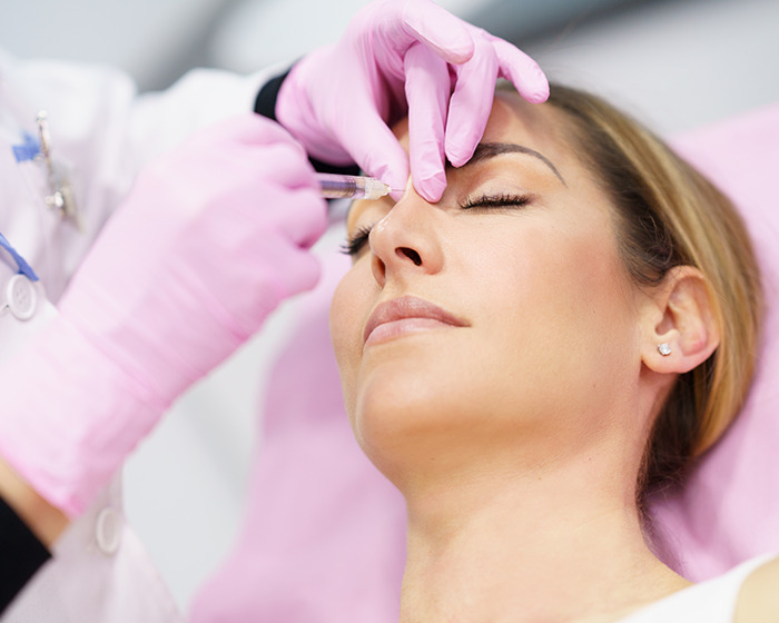 Woman receiving cosmetic injection near eyes from gloved medical professional in a clinical setting, highlighting mom wakes from surgery story. Woman receiving cosmetic injection near eyes from gloved medical professional in a clinical setting, highlighting mom wakes from surgery story.