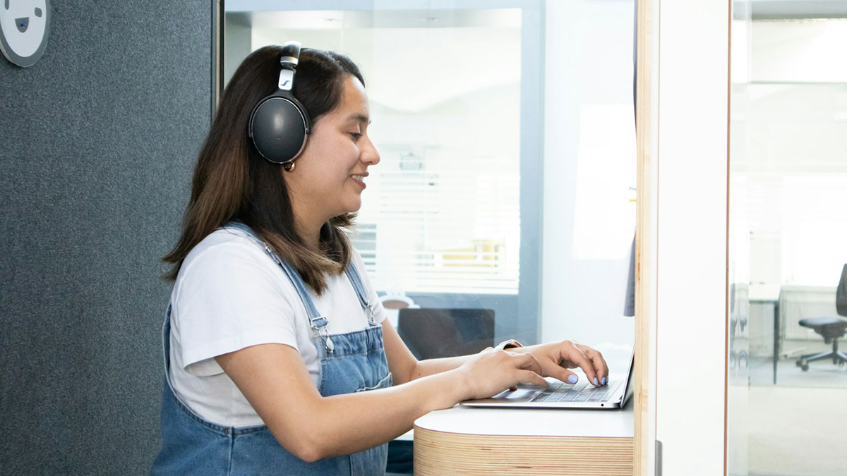 Woman wearing headphones working on a laptop in an office, related to jobs that shouldnu2019t be earning as much as they do