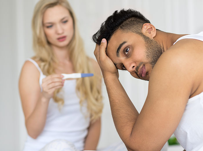 Man looks stressed while woman holds a positive pregnancy test, depicting challenges of raising a newborn alone. Man looks stressed while woman holds a positive pregnancy test, depicting challenges of raising a newborn alone.