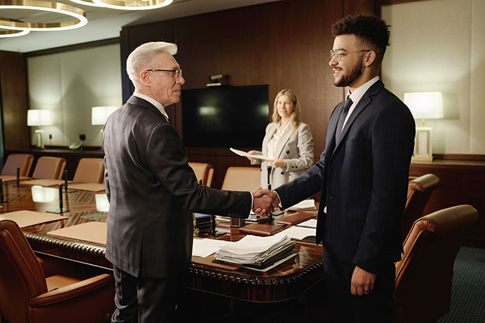 Two men in suits shaking hands in a conference room while a woman observes in a professional setting about man raising newborn alone. Two men in suits shaking hands in a conference room while a woman observes in a professional setting about man raising newborn alone.