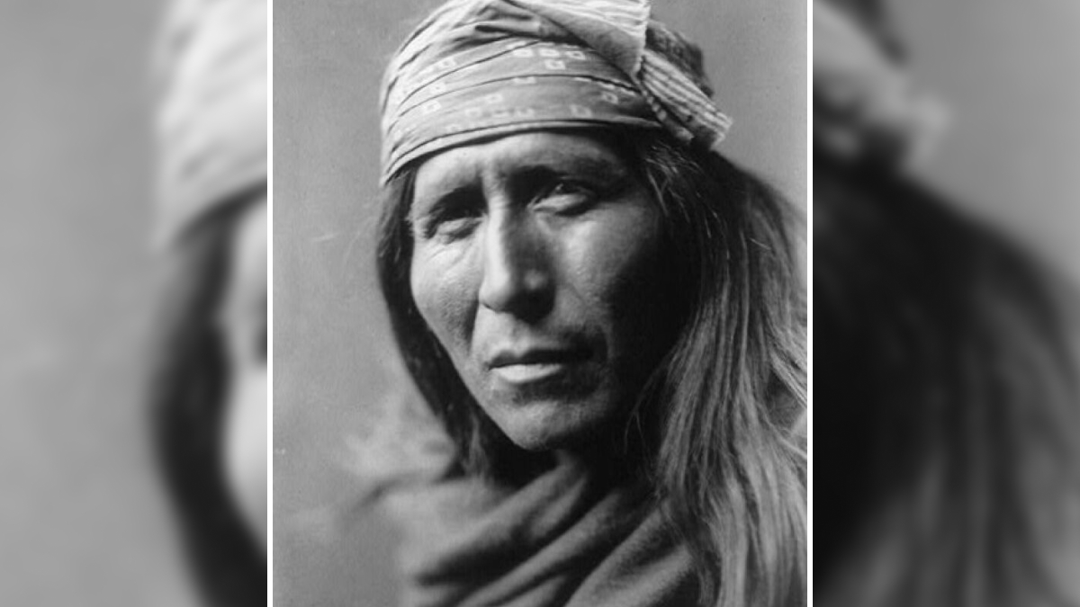 Native American man wearing a patterned headband and traditional clothing, revealing life in the 1900s.