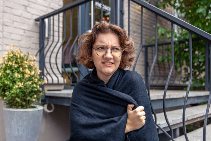 Woman wrapped in a blanket with a skeptical expression sitting near stairs, illustrating entitled lady parking dispute and rumor spreading. Woman wrapped in a blanket with a skeptical expression sitting near stairs, illustrating entitled lady parking dispute and rumor spreading.