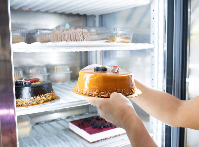 Person placing a caramel birthday cake in a refrigerator, relating to lady excluding nephew from son's birthday party. Person placing a caramel birthday cake in a refrigerator, relating to lady excluding nephew from son's birthday party.
