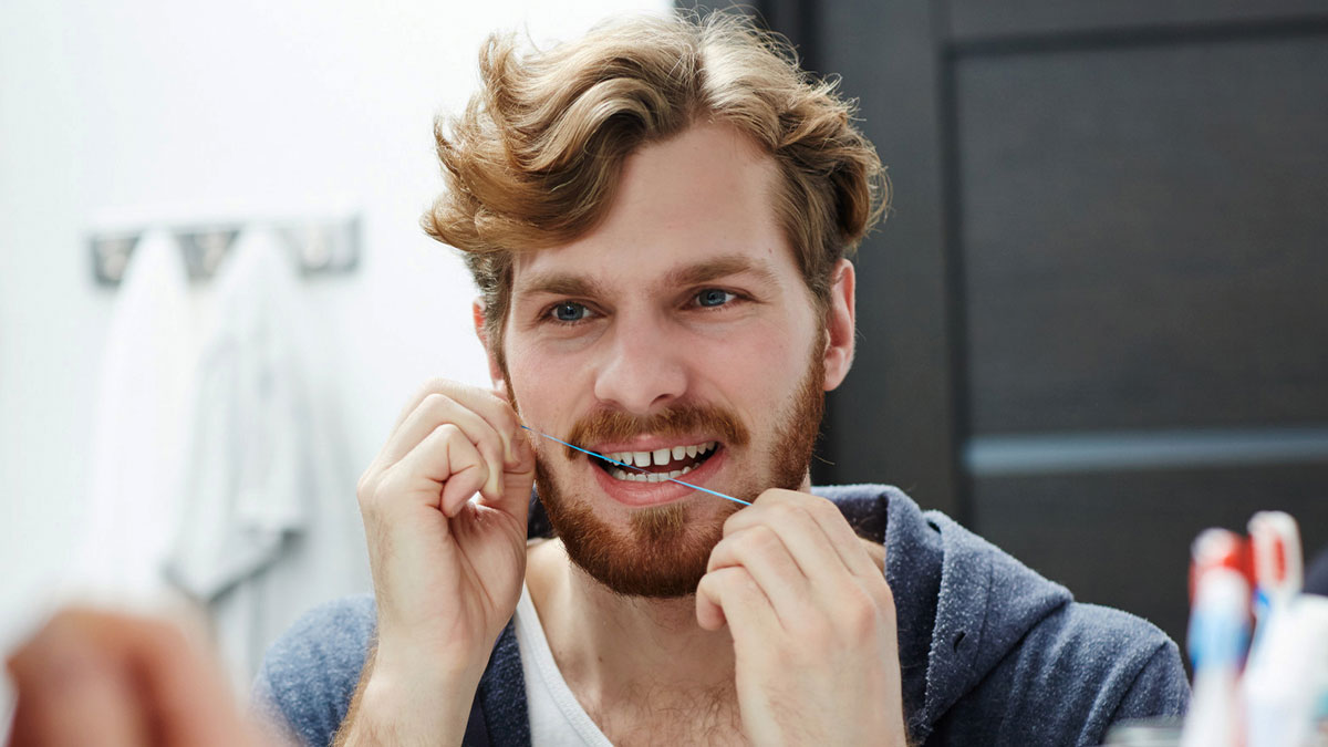 Man with fake teeth flossing in bathroom mirror, highlighting trust issues in a long-term relationship.