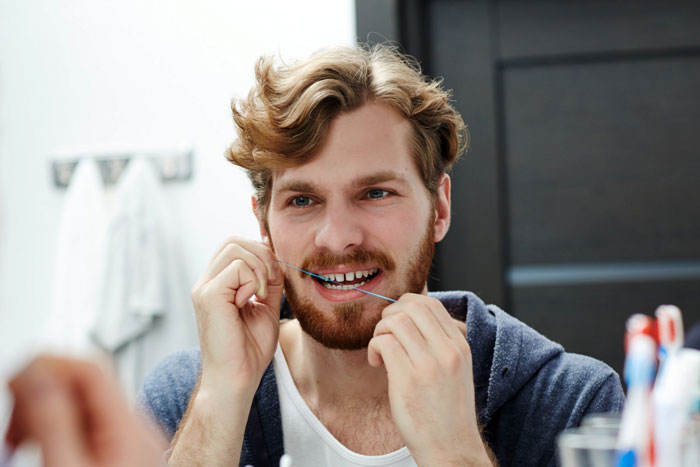 Man flossing teeth in bathroom mirror, symbolizing man tells girlfriend his teeth aren’t real after years together trust issues.