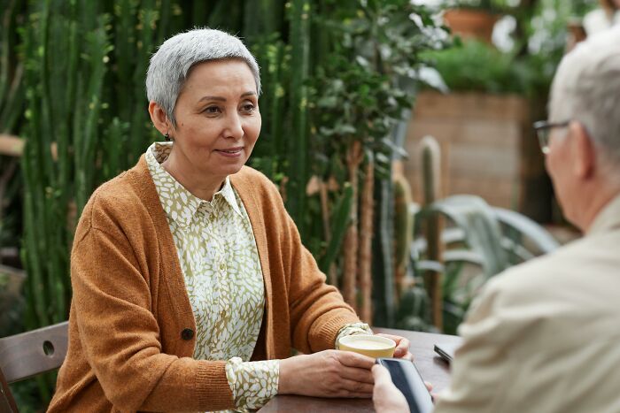 Mature woman in a cozy sweater having a serious conversation over coffee, hinting at new romance concerns.