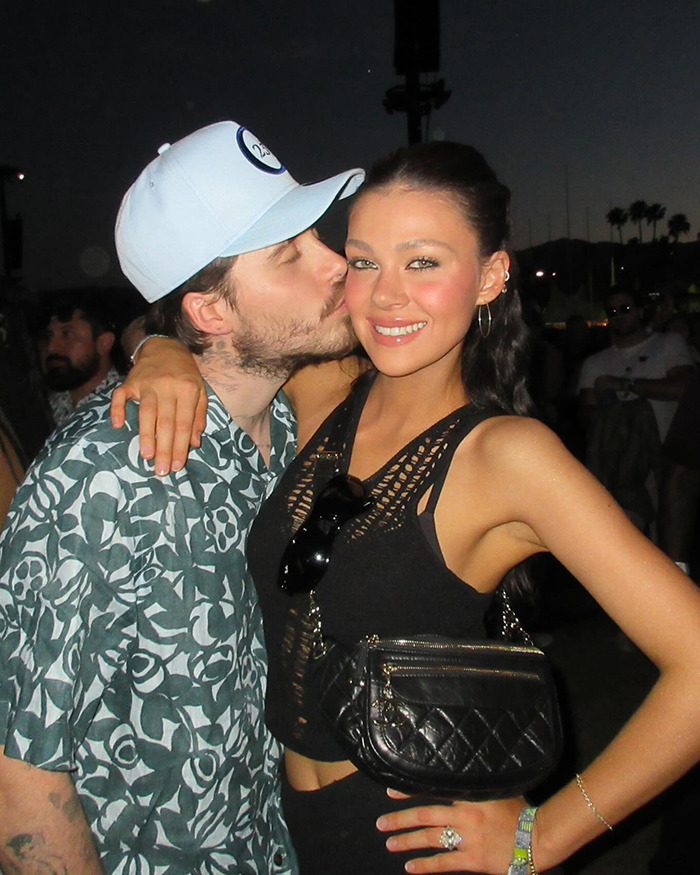 Nicola Peltz smiling while man kisses her cheek outdoors at night, related to David Beckham narcissistic family feud news. Nicola Peltz smiling while man kisses her cheek outdoors at night, related to David Beckham narcissistic family feud news.