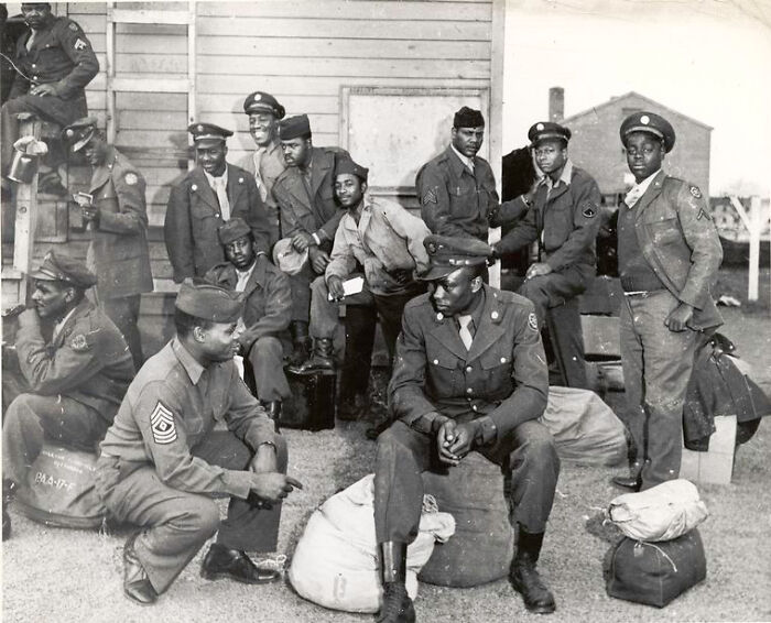 Group of African American soldiers in uniform gathered outdoors with their military bags around them in historical photo