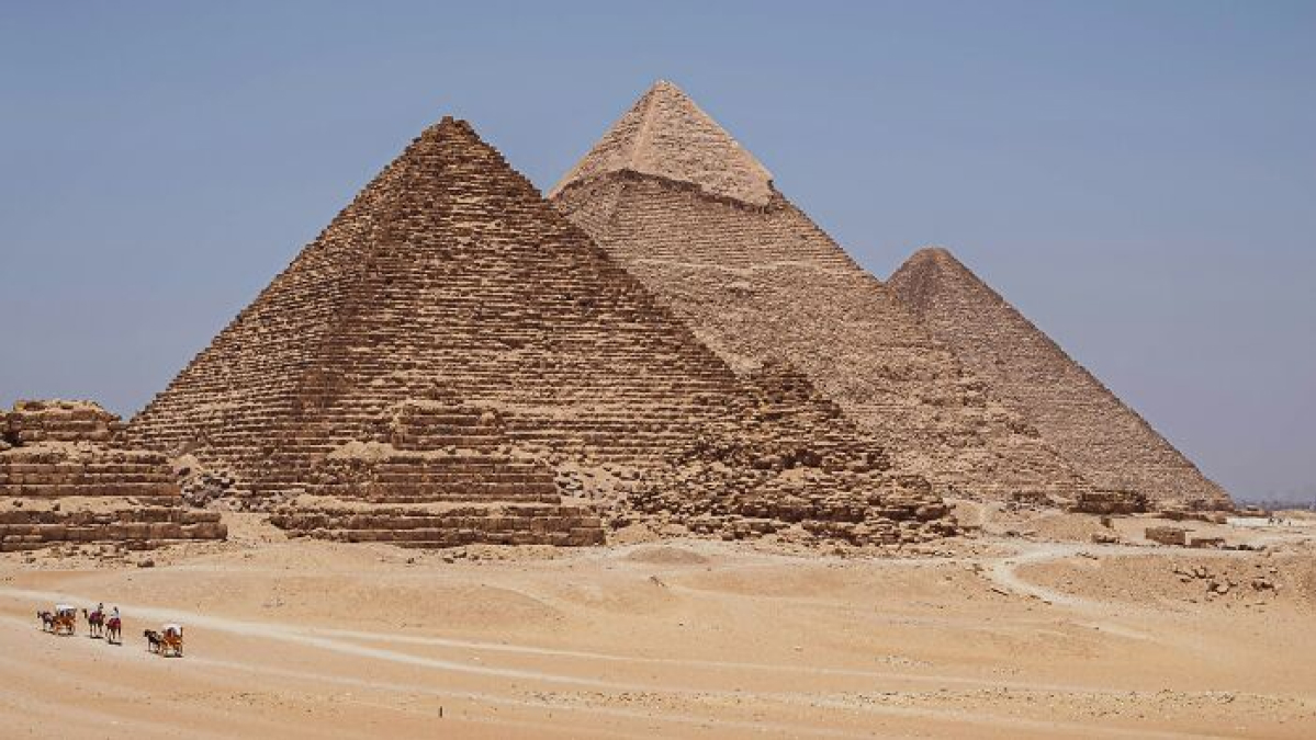 Ancient man-made structures of the Egyptian pyramids standing tall in the desert under a clear blue sky.