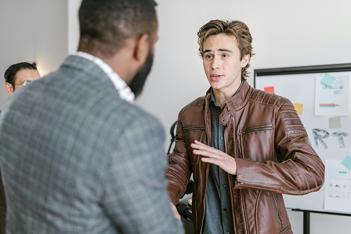 Young worker in a brown leather jacket discussing the one minute late rule with his boss in an office setting. Young worker in a brown leather jacket discussing the one minute late rule with his boss in an office setting.