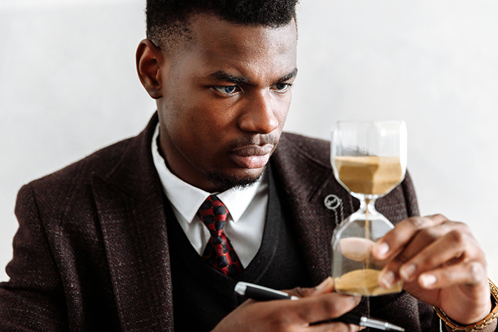 Man in suit holding hourglass, symbolizing strict enforcement of one minute late rule by boss at workplace. Man in suit holding hourglass, symbolizing strict enforcement of one minute late rule by boss at workplace.