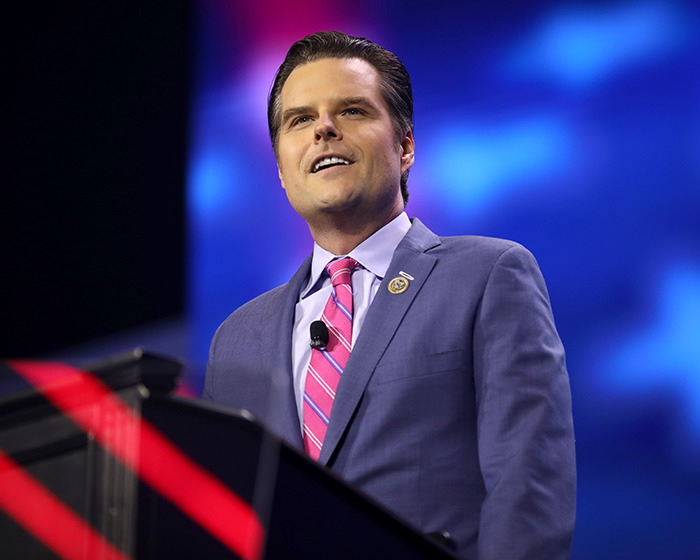 Man in a suit and pink tie speaking at a podium, illustrating plastic surgeons revealing secrets behind Mar-a-Lago face. Man in a suit and pink tie speaking at a podium, illustrating plastic surgeons revealing secrets behind Mar-a-Lago face.