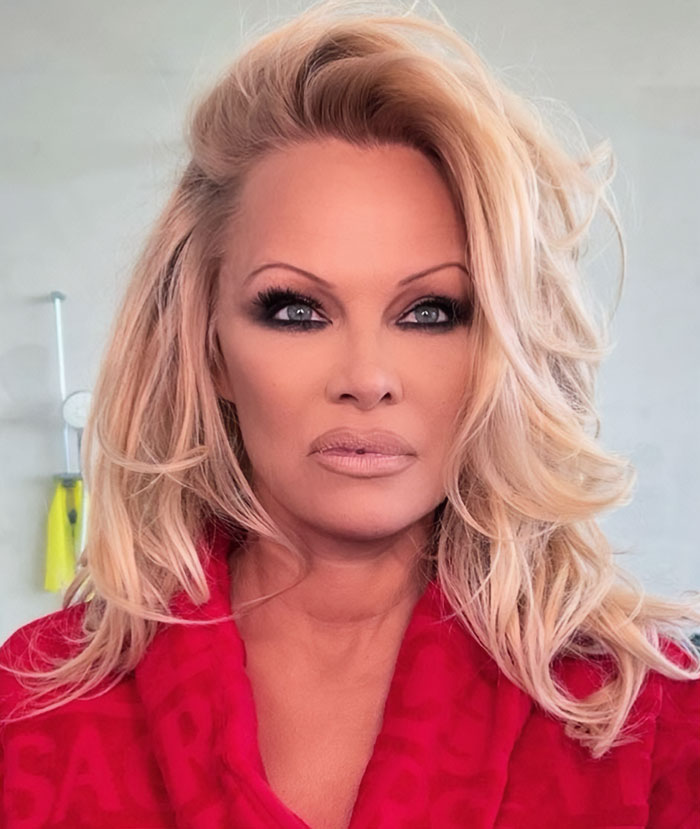 Pamela Anderson with 90s glam makeup look featuring bold eye makeup and voluminous blonde hair in a red robe. Pamela Anderson with 90s glam makeup look featuring bold eye makeup and voluminous blonde hair in a red robe.
