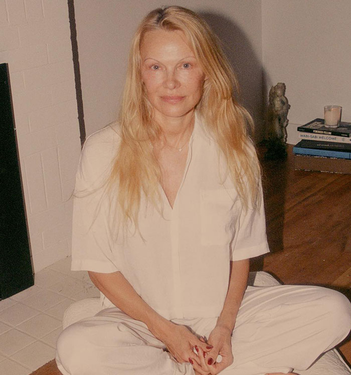 Pamela Anderson sitting cross-legged indoors, showcasing a natural look after years before 90s glam makeup return. Pamela Anderson sitting cross-legged indoors, showcasing a natural look after years before 90s glam makeup return.