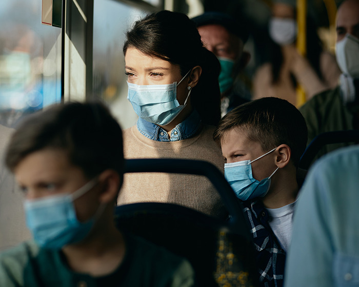 Three children wearing medical masks indoors looking out a window with serious expressions on public transport. Three children wearing medical masks indoors looking out a window with serious expressions on public transport.