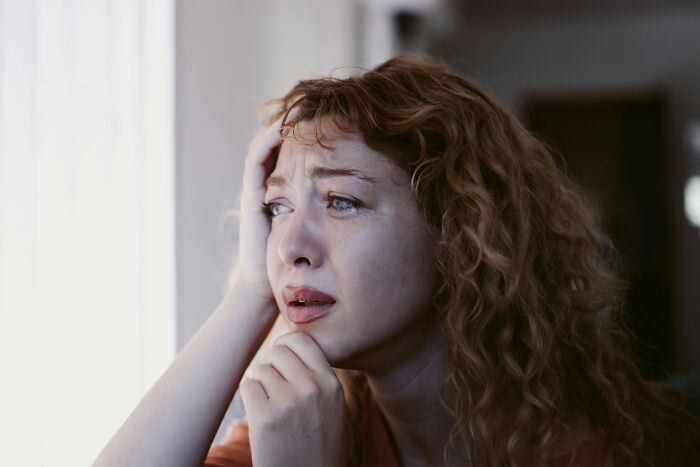 Sad woman with curly hair looking out window, highlighting teen desperate to say goodbye to sick father emotions. Sad woman with curly hair looking out window, highlighting teen desperate to say goodbye to sick father emotions.