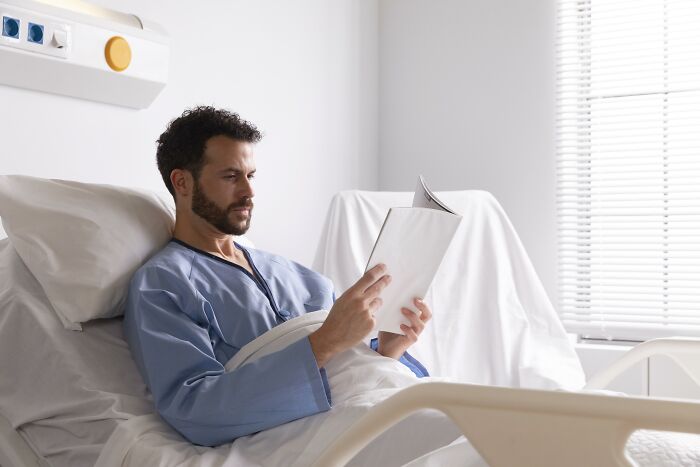 Man in hospital gown reading a book in bed, illustrating spooky tales of people passing away and being resurrected.