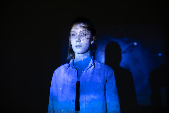 Young woman illuminated by blue light projection, evoking eerie and spooky tales of resurrection and time travel.