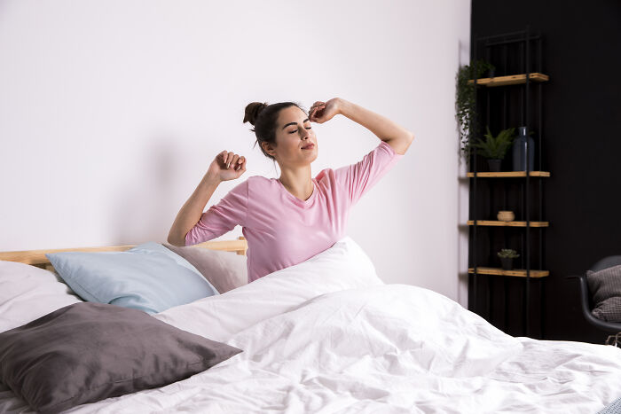 Young woman stretching in bed after waking up, symbolizing stories of people passing away but being resurrected.