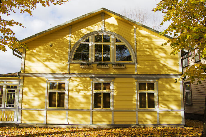 Yellow wooden house with large windows surrounded by autumn trees, evoking spooky tales of resurrection and time travel.