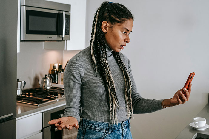 Woman in kitchen looking frustrated at phone, reacting to husband guarding box of olives like precious gold. Woman in kitchen looking frustrated at phone, reacting to husband guarding box of olives like precious gold.