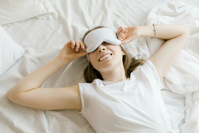 Young woman relaxing on bed with sleeping mask, showing a tiny thing that made trip better by enhancing rest.