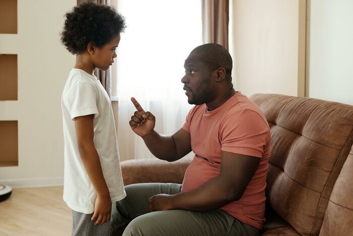 Father sitting on couch lecturing child standing in living room, illustrating absurd things people were told growing up.