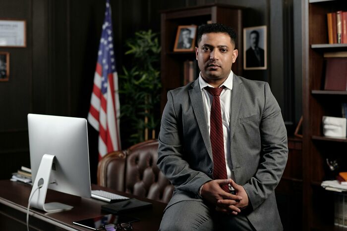 Man in a suit sitting on a desk in an office with a computer, representing tech guys fixing customer computers.
