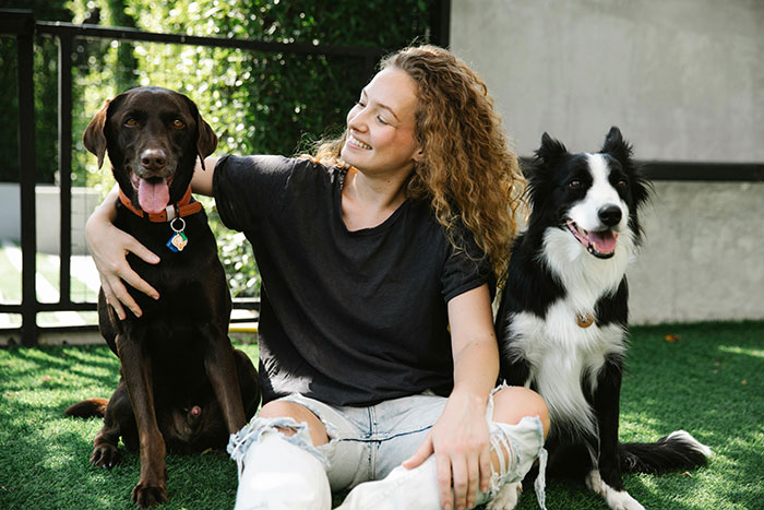 Young dog mom sitting on grass with two dogs, showing bond and seeking equal treatment as moms with kids Young dog mom sitting on grass with two dogs, showing bond and seeking equal treatment as moms with kids