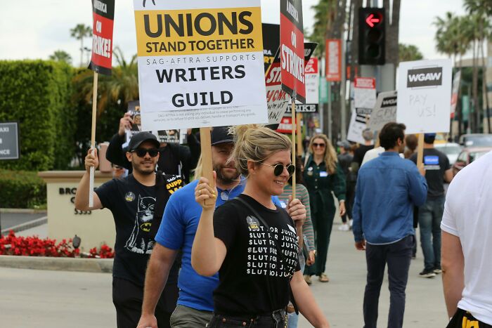 Protesters holding signs at a writers guild strike, highlighting unions as a key absurd thing people once agreed with.