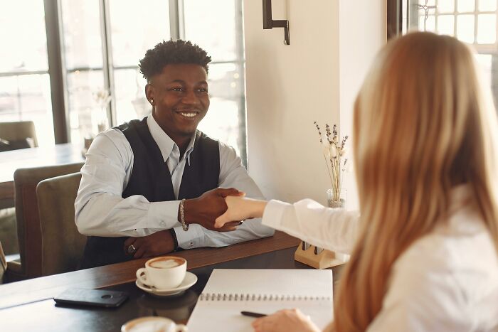 Two employees shaking hands during a job interview discussing strange and dumb recruiter experiences in an office setting.