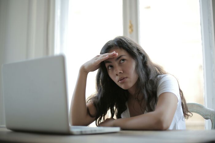 Young woman looking annoyed while working on a challenging test with 23 questions on her laptop at a bright table Young woman looking annoyed while working on a challenging test with 23 questions on her laptop at a bright table