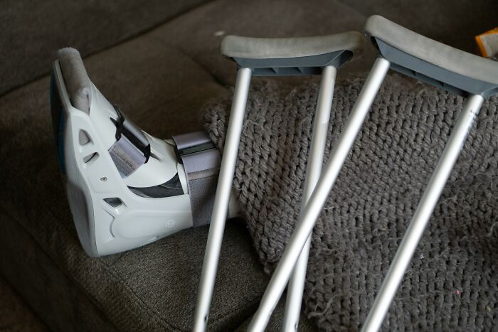 Person's leg in medical walking boot with crutches resting on a couch illustrating absurd things told growing up.