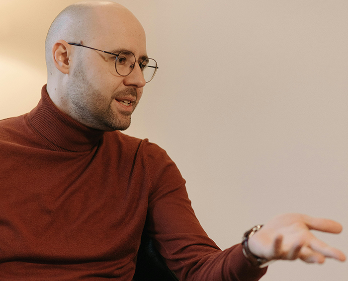 Man in glasses and a red turtleneck expressing strong emotions while discussing grandbaby as a sign from late wife. Man in glasses and a red turtleneck expressing strong emotions while discussing grandbaby as a sign from late wife.