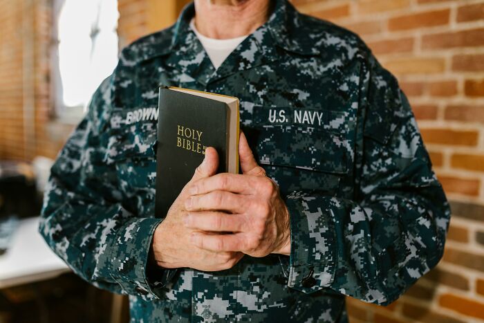 Person in U.S. Navy uniform holding a Holy Bible, illustrating people share companies bad list concerns.