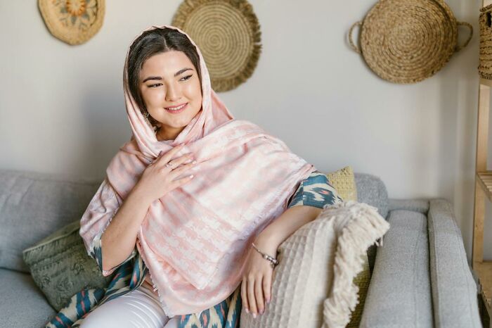 Woman wearing a traditional headscarf sitting on a couch, representing cultural aspects in national stereotypes.