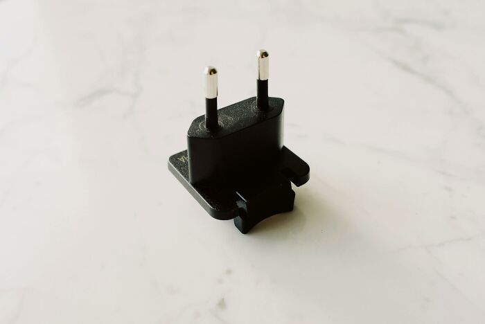 Black travel adapter plug on a white surface showing a tiny thing that made the trip better for easy charging.