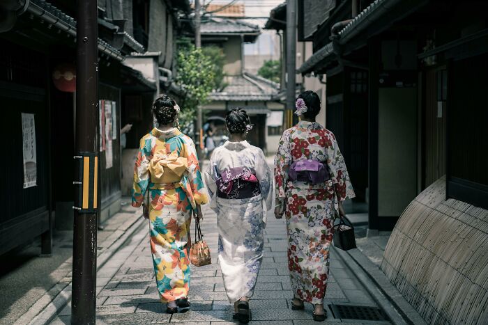 Three women in traditional kimonos walking down a narrow street, illustrating national stereotypes and cultural attire.