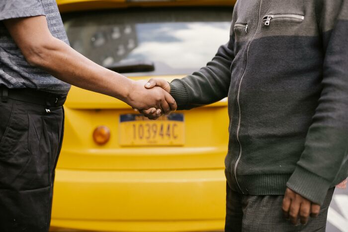 Two people shaking hands in front of a yellow vehicle, illustrating absurd things people were told growing up.