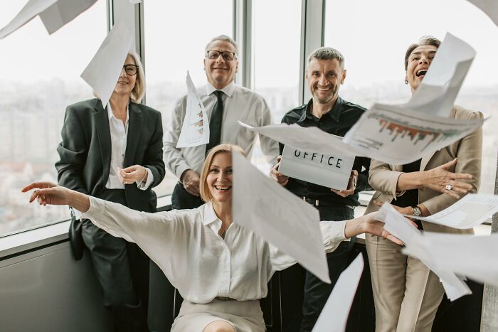 Group of office workers smiling and throwing papers, illustrating absurd things people were told growing up that they now disagree with