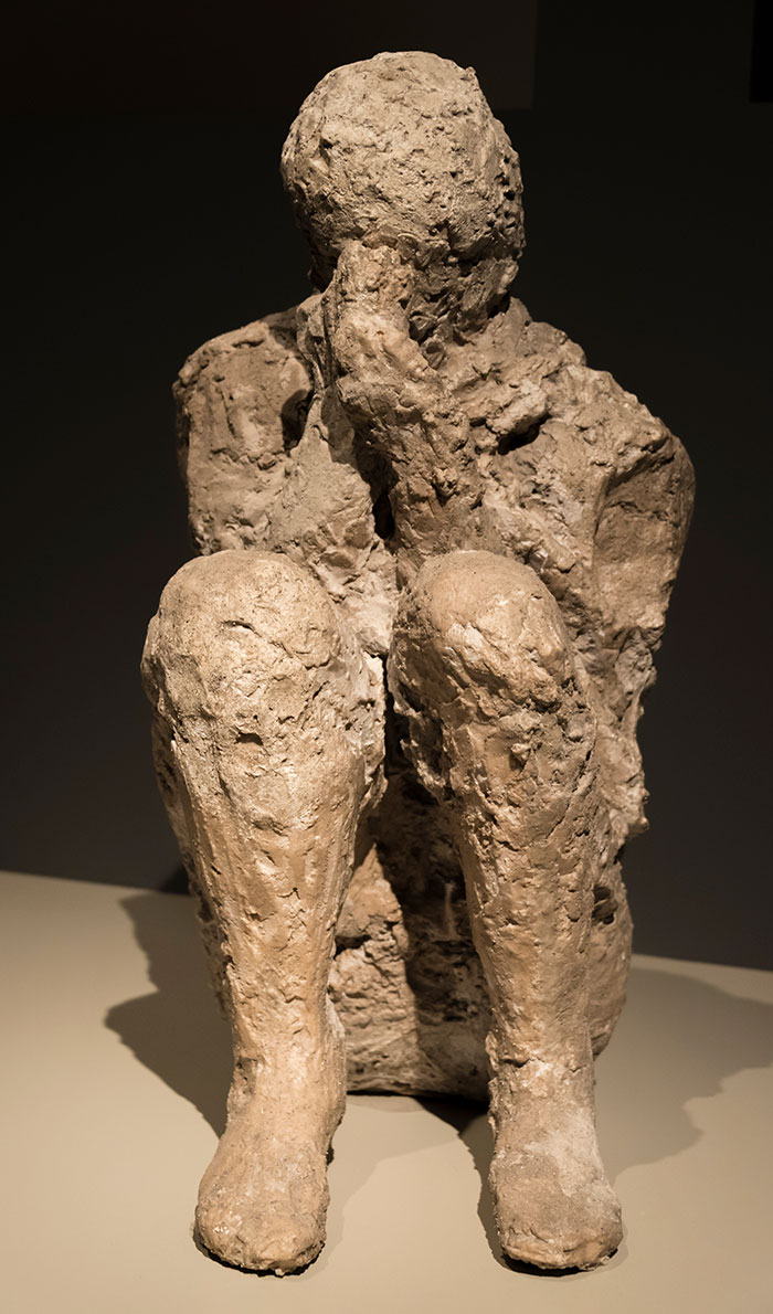 Pompeii plaster cast of a seated figure shielding face, revealing parents' tragic attempt to protect child in volcanic disaster. Pompeii plaster cast of a seated figure shielding face, revealing parents' tragic attempt to protect child in volcanic disaster.