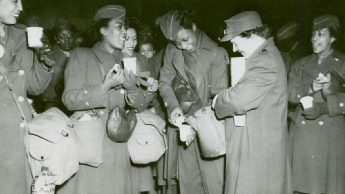 African American women in military uniform sharing food and drinks, showcasing unity and history in uniform.