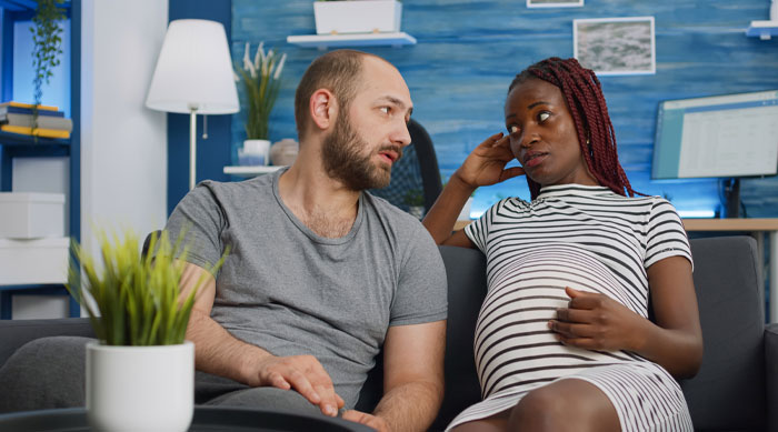 Pregnant wife and husband discussing pregnancy after vasectomy, sitting on couch in a modern living room.