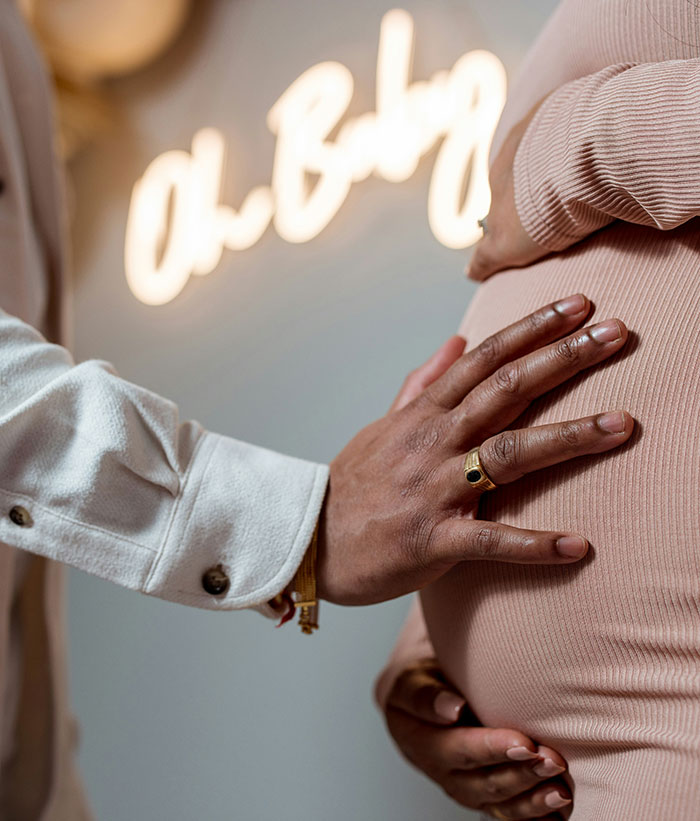 Man's hand on pregnant wife's belly during baby gender reveal celebration, highlighting tension with mom nearby.