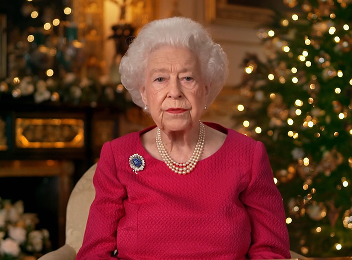 Queen Elizabeth in a formal setting, wearing a red dress and pearl necklace, related to Meghan Markle wedding caterer incident. Queen Elizabeth in a formal setting, wearing a red dress and pearl necklace, related to Meghan Markle wedding caterer incident.